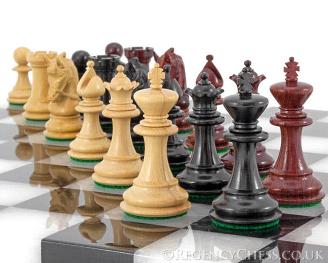 Luxury Corinthian Tres Corone chess pieces in exotic woods on a chessboard, featuring handcrafted 2.5-inch Staunton design with billiard cloth bases.